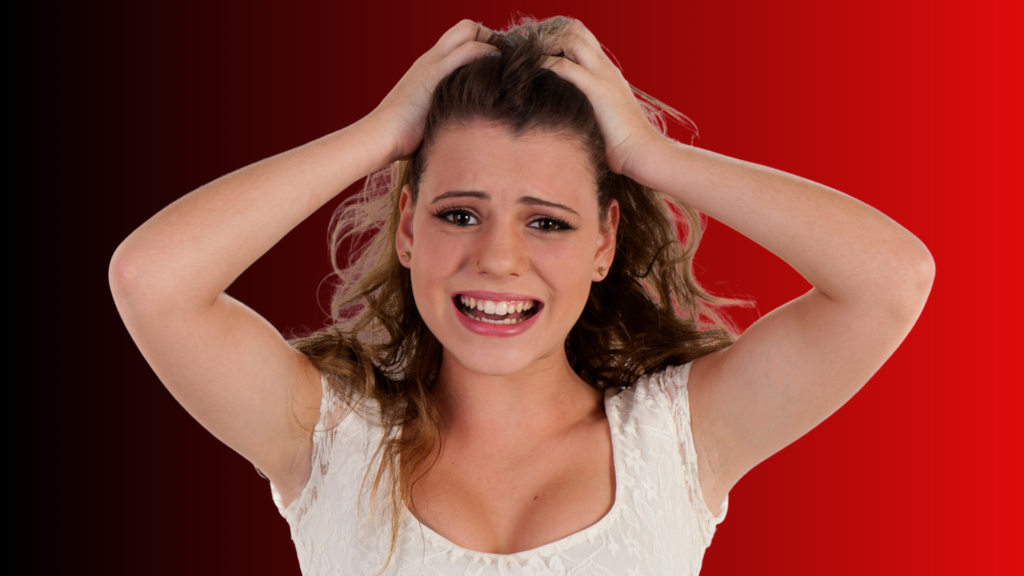 Mulher com expressão de desespero, puxando os cabelos e transmitindo ansiedade, em um fundo vermelho que intensifica a sensação de tensão emocional por não saber como fazer ele pensar em você.