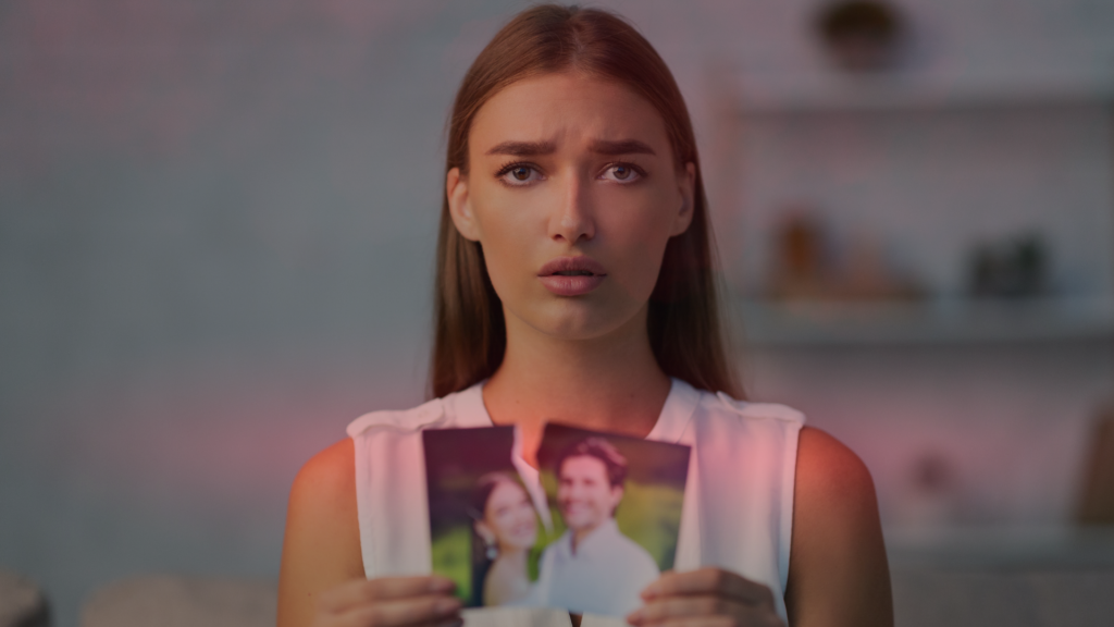 Mulher com expressão triste segurando uma foto rasgada de um casal, sugerindo o fim de uma relação e não saber como fazer ele pensar em você.