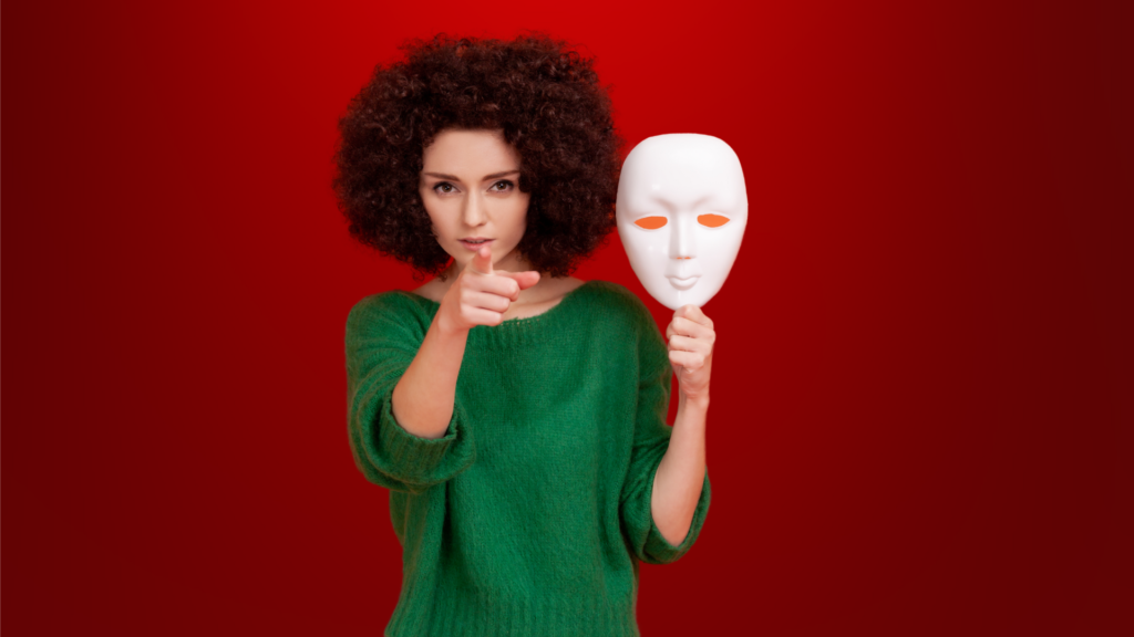 Mulher com expressão determinada, apontando diretamente para a câmera enquanto segura uma máscara branca ao lado, representando a ideia de revelar a verdade e desmascarar falsos líderes espirituais.