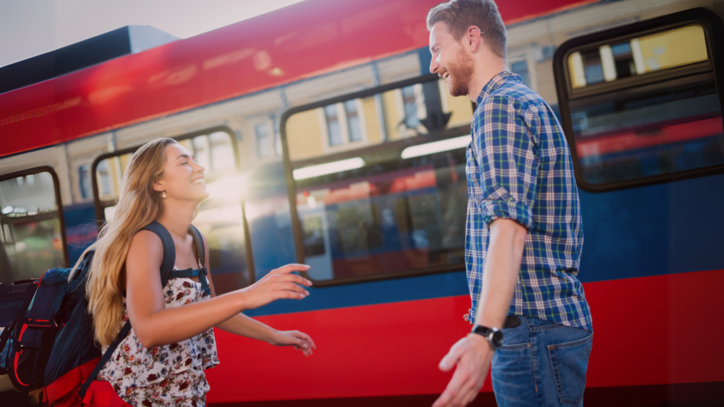 Casal sorridente se reencontrando em uma estação de trem, com os braços abertos em um gesto de felicidade e conexão emocional, simbolizando uma nova chance ou reconciliação.