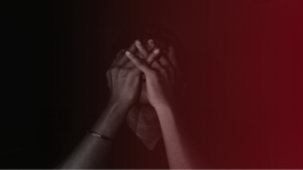 Uma pessoa em um ambiente escuro, cobrindo o rosto com as mãos, simbolizando sentimentos de estagnação, frustração ou busca de resolução para problemas emocionais ou financeiros.