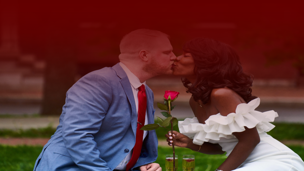 Imagem de um casal sentado em um parque, compartilhando um momento romântico enquanto se beijam. A mulher segura uma rosa vermelha e ambos estão vestidos elegantemente, com taças de champanhe ao fundo, simbolizando como melhorar seu relacionamento depois do Selamento.