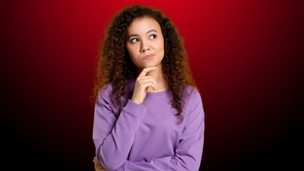 Mulher jovem de cabelos cacheados e expressão pensativa, com a mão no queixo, olhando para o lado como se refletisse sobre como conseguir um compromisso sincero. O fundo em tons de vermelho escuro adiciona um ar de intensidade e questionamento à cena.