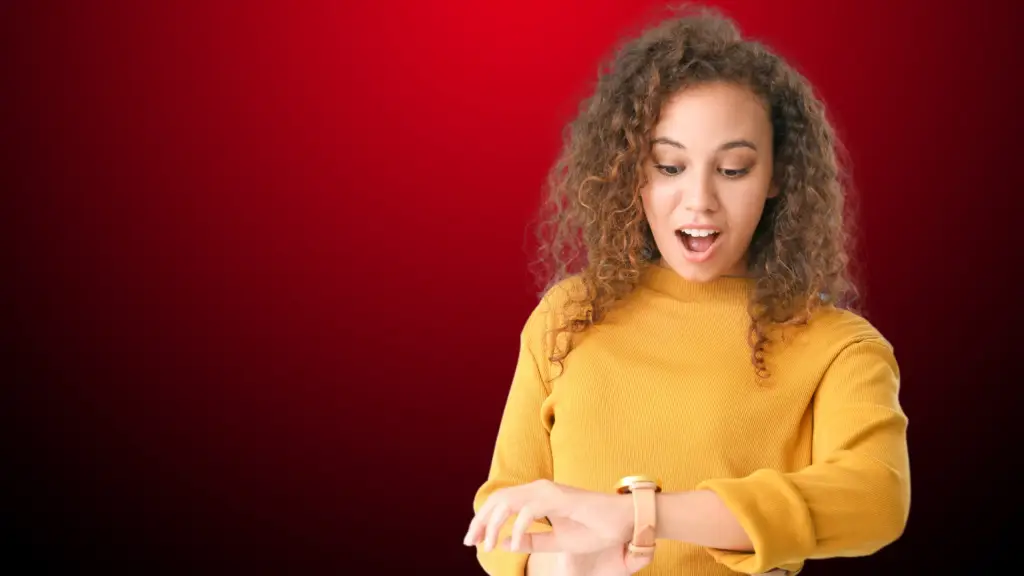 Mulher com expressão surpresa e animada olha para o próprio relógio de pulso. Ela usa blusa amarela e está sobre um fundo em degradê vermelho escuro. A cena remete à ideia de tempo ou contagem regressiva, simbolizando quanto tempo dura um simbolizando o relacionamento rebote.