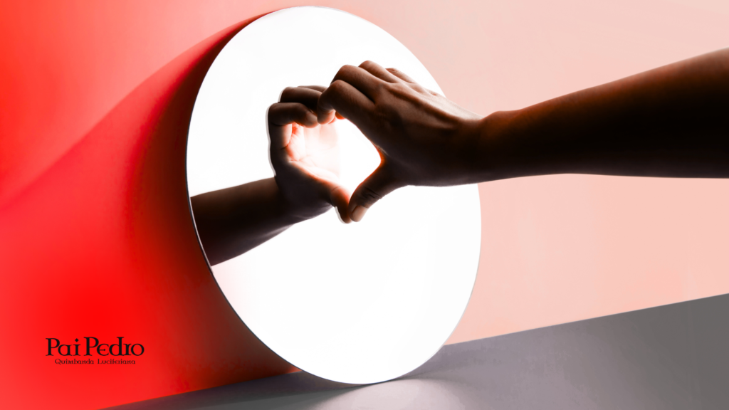 Mãos formando um coração diante de um espelho redondo iluminado, simbolizando o ato de autoconhecimento e amor próprio durante a fase da solteirice. Fundo em tons suaves de vermelho e rosa, transmitindo um clima introspectivo e de autoaceitação.