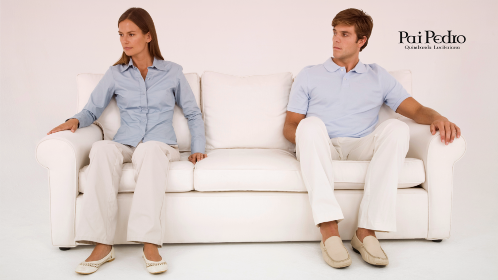 Casal sentado em um sofá branco, visivelmente distante um do outro, sem contato físico ou visual, com expressões fechadas e postura rígida. Representa simbolicamente o distanciamento emocional ou a iminência de uma separação afetiva.