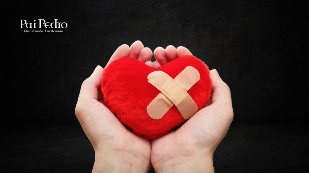 Duas mãos seguram com delicadeza um coração de pelúcia vermelho, machucado com dois curativos cruzados no centro, transmitindo a ideia de feridas emocionais. O fundo é preto e o logotipo "Pai Pedro - Quimbanda Luciferiana" aparece no canto superior esquerdo.