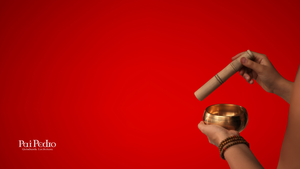 Mãos segurando um sino tibetano dourado sobre fundo vermelho, simbolizando a preparação e ativação espiritual em um ritual de prosperidade com Ogum.