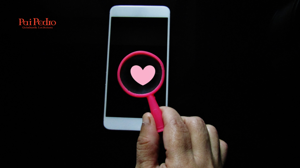 Mão segurando lupa rosa sobre celular com coração, simbolizando a busca por manter um webnamoro vivo e cheio de amor.
