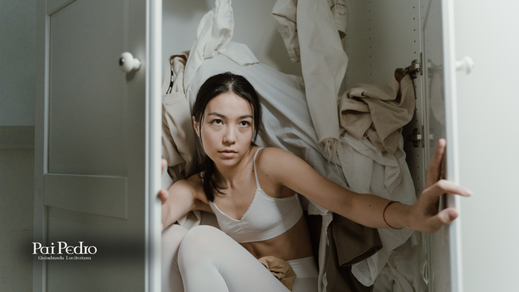 Mulher encolhida dentro de um armário, cercada por roupas, com olhar distante — metáfora visual para o isolamento emocional causado pela carência afetiva.