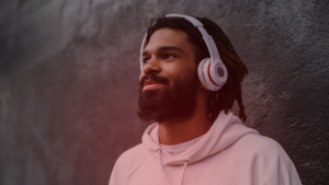 Homem usando fones de ouvido, perdido em pensamentos e olhando para o horizonte com um leve sorriso no rosto, sugerindo que uma música trouxe à mente lembranças de alguém especial. Algo que faz como fazer ele pensar em você