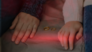 Mãos de um casal repousam sobre uma superfície com duas alianças entre elas, simbolizando um momento de crise no relacionamento. A imagem transmite sentimentos de crises no relacionamento