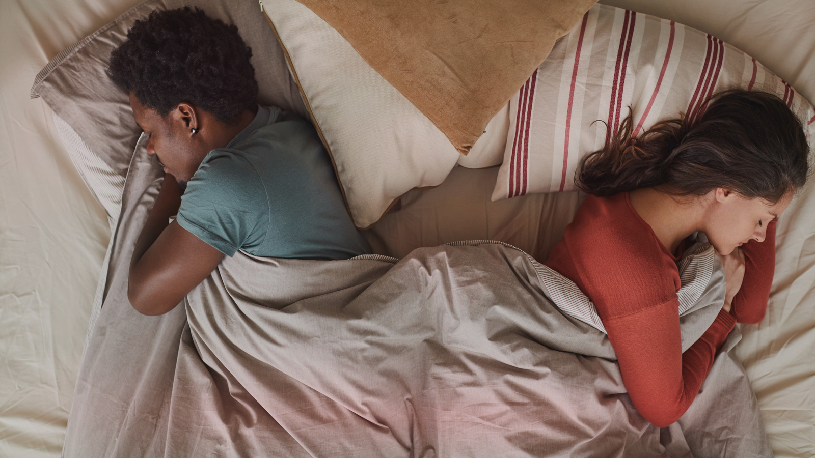 Casal deitado na cama, de costas um para o outro, demonstrando que o relacionamento esfriou. Ambos cobertores pelo edredom, com expressões serenas, mas indicando falta de conexão.