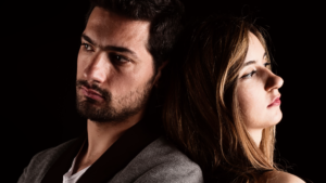 Homem e mulher sentados de costas um para o outro, com expressões sérias e distantes, sugerindo um conflito ou distanciamento emocional. O fundo escuro realça o contraste entre os dois, reforçando a sensação de frustração ou desentendimento no relacionamento sério