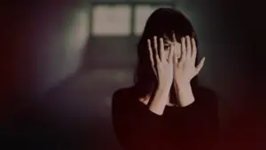 Mulher em um ambiente escuro cobrindo o rosto com as mãos, simbolizando o sentimento de aprisionamento emocional e a dificuldade de enxergar uma saída em um relacionamento tóxico..
