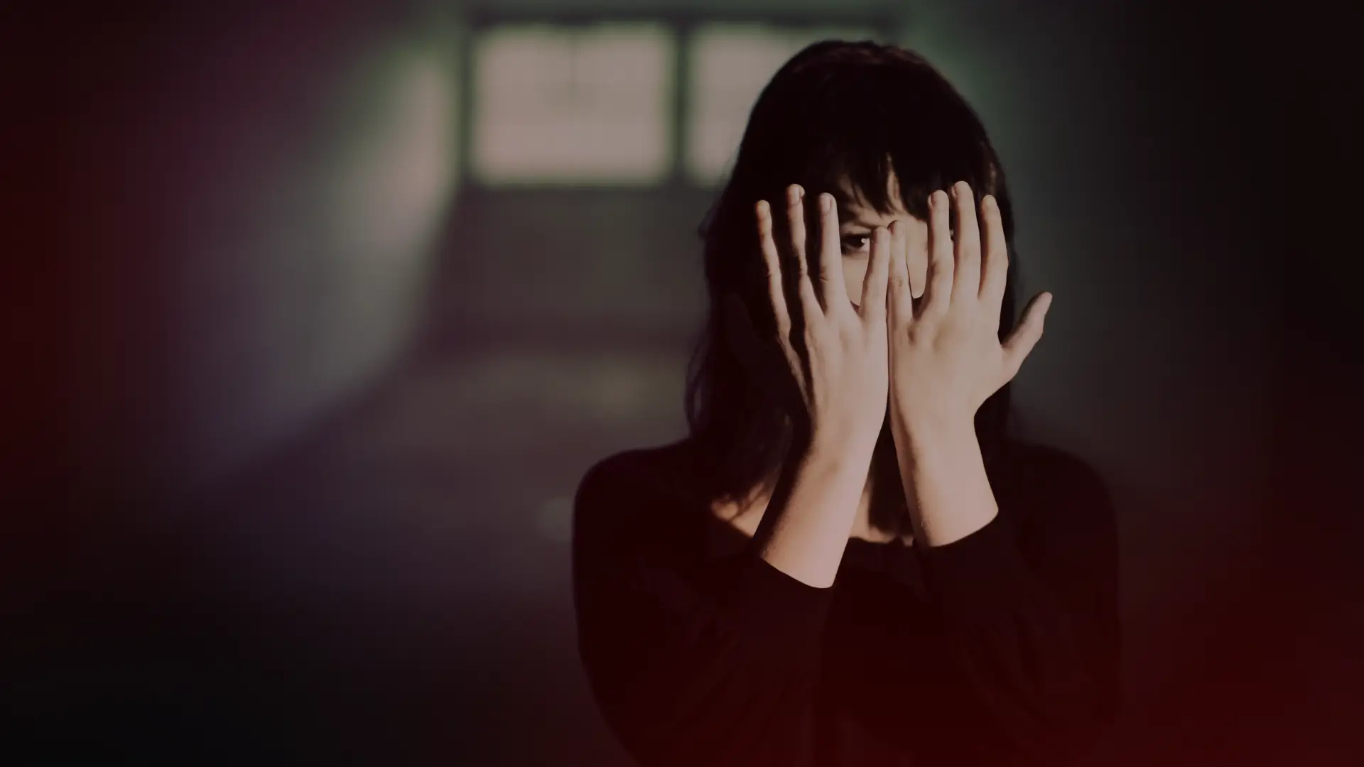 Mulher em um ambiente escuro cobrindo o rosto com as mãos, simbolizando o sentimento de aprisionamento emocional e a dificuldade de enxergar uma saída em um relacionamento tóxico..