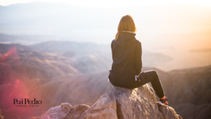 Mulher sentada em um penhasco, contemplando o horizonte ao pôr do sol. A imagem transmite um momento de reflexão e autoconhecimento, simbolizando a liberdade da solteirice — uma fase que assusta, mas também liberta.